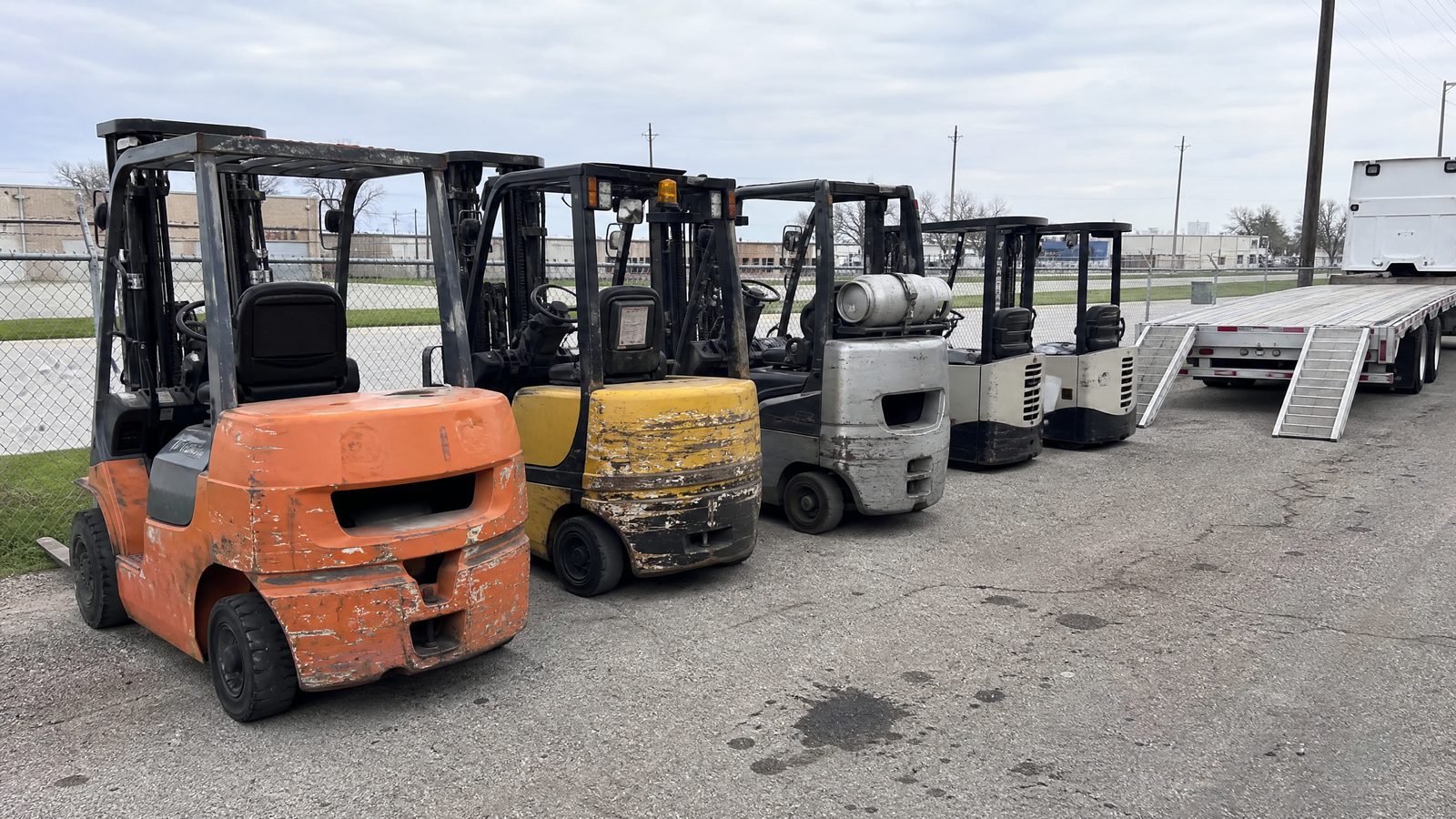 Row of used forklifts staged beside a flatbed trailer after a fleet purchase