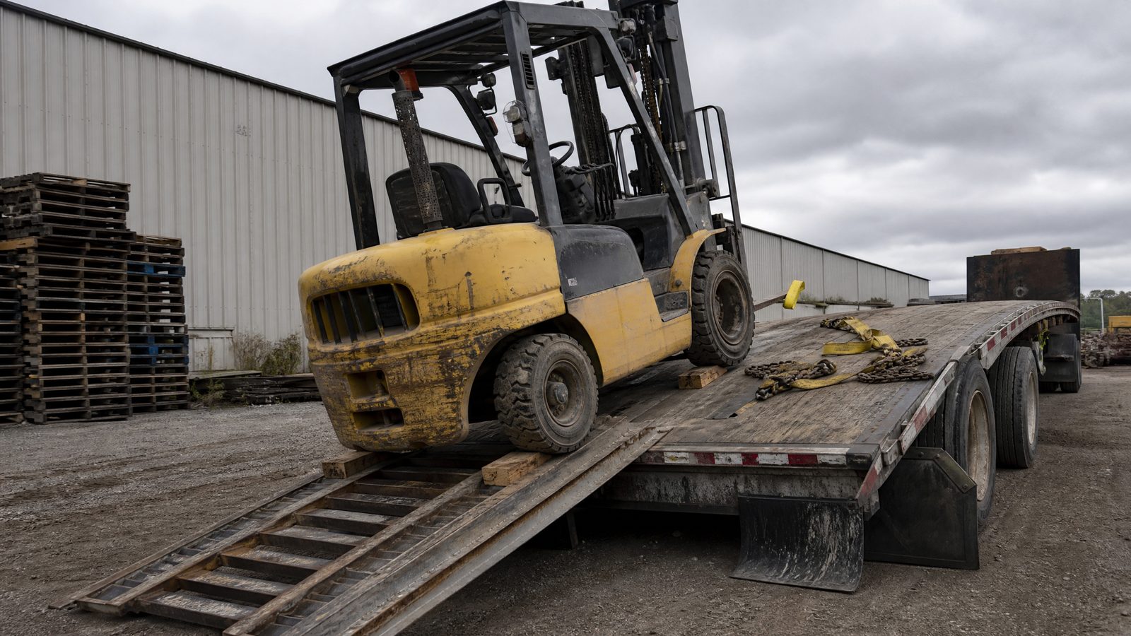 Used yellow forklift loaded and chained on a flatbed trailer at our cost after purchase